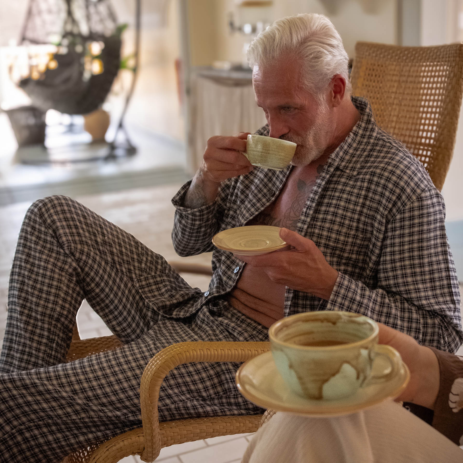 En äldre man sitter i en fåtölj och dricker ur en kopp.