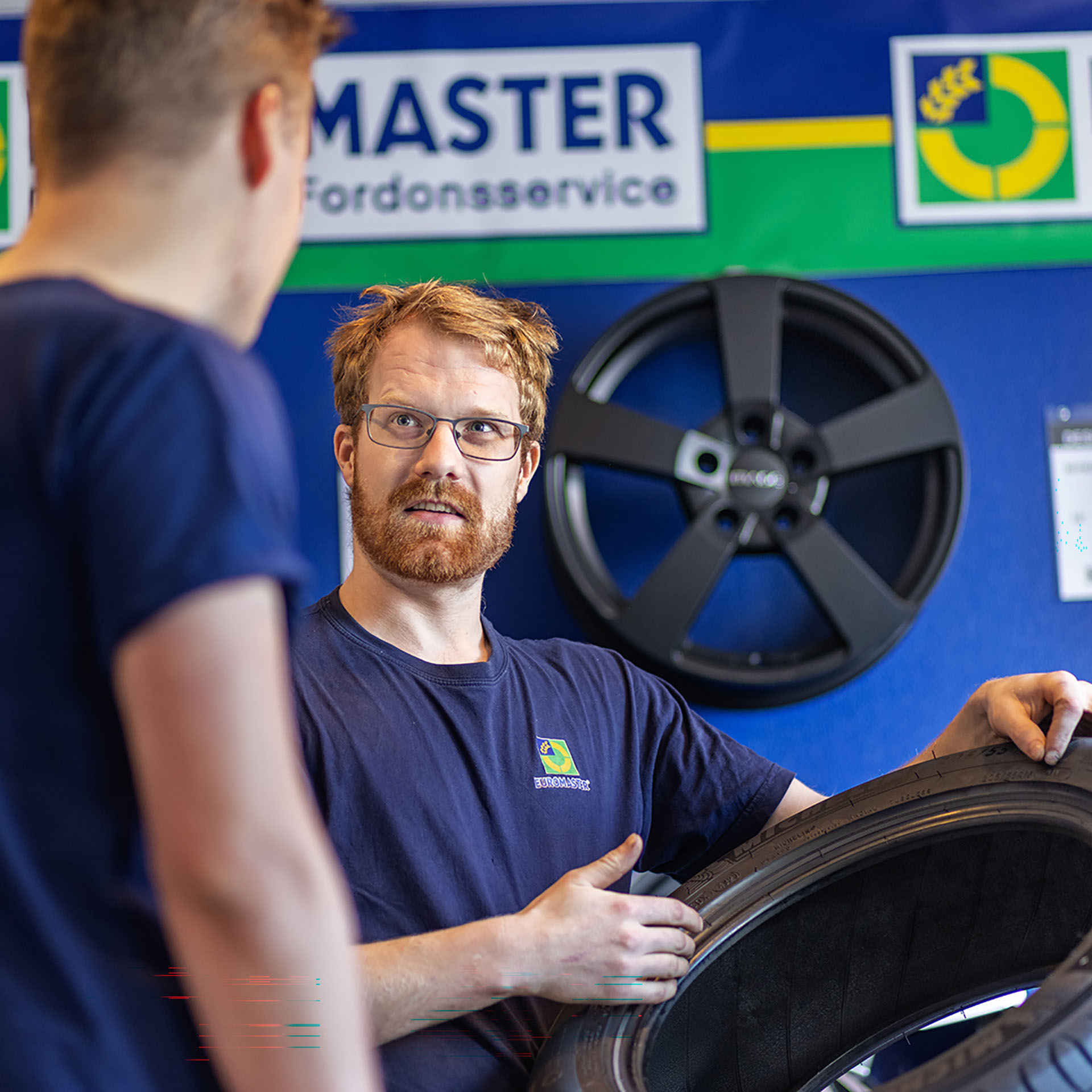 En bilmekaniker visar upp ett däck för en annan person.