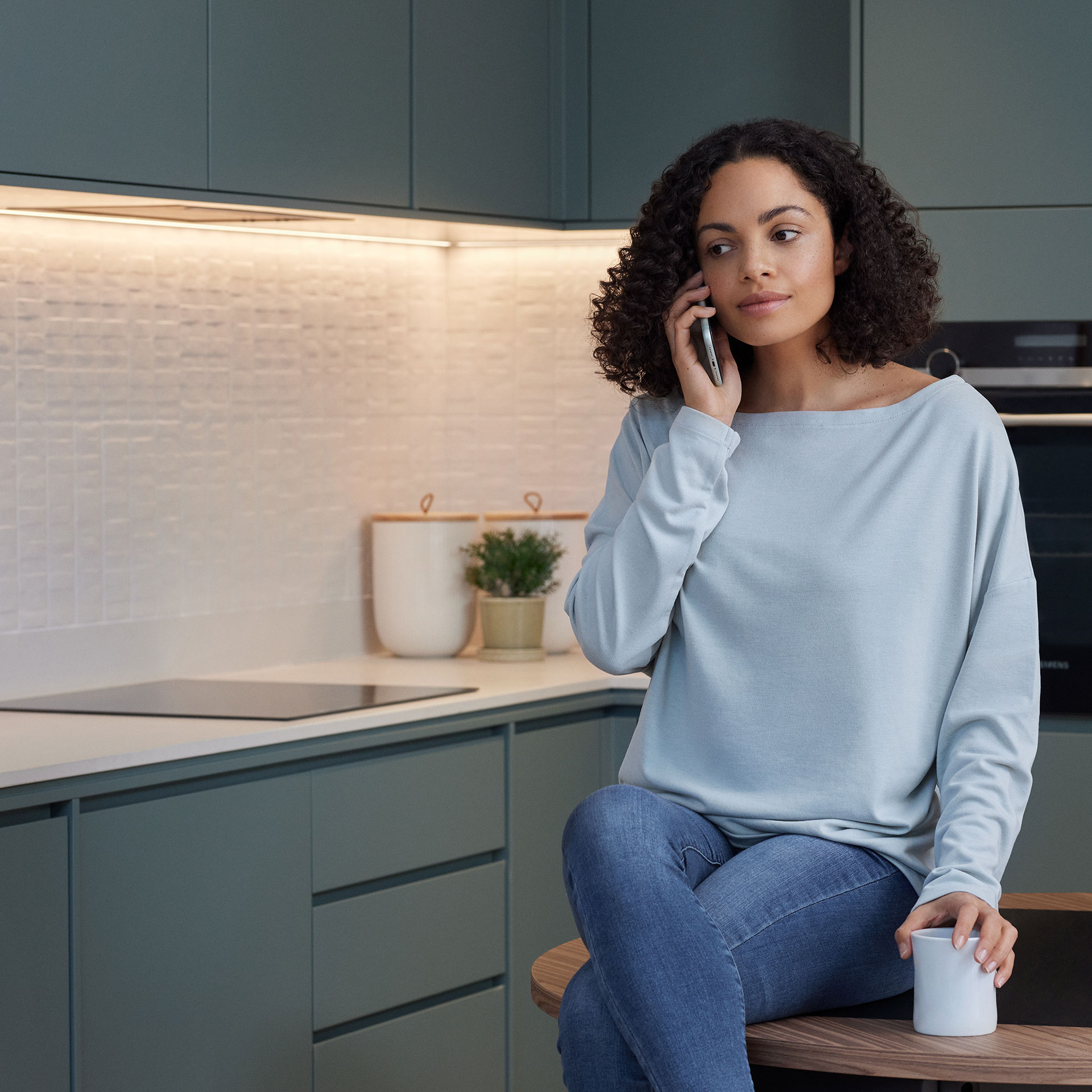 En mörkhårig kvinna pratar i telefon i ett kök.