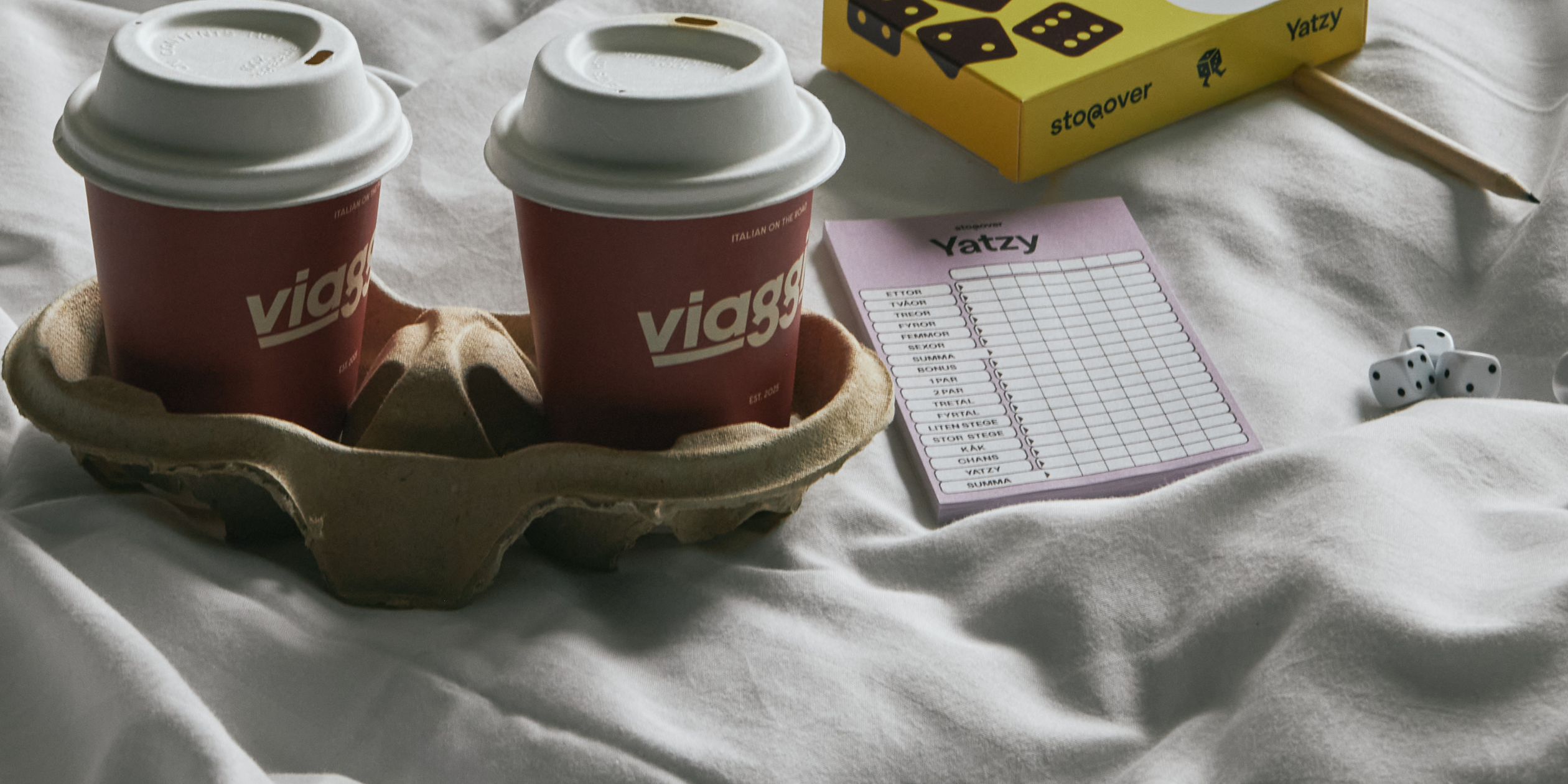 Två muggar och Yatzy på en säng. Stopover.