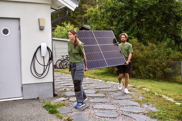 Kvinna och man bär på en solcellspanel utanför ett hus